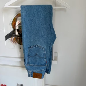 Levi's 70s High Slim Straight jeans blå - Säljer ett par Levi's 70s High Slim Straight jeans i klassisk ljusblå denim. Hög midja, raka ben och slim passform. Snygga detaljer med fem fickor, silverfärgade nitar och Levi's läderpatch bak. Perfekta för en avslappnad och trendig look. Storlek 25/32.