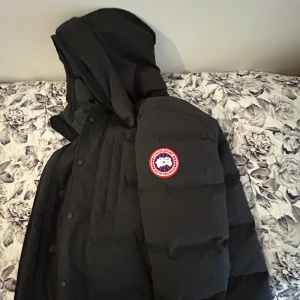 Carson parka från Canada Goose i XS (ÄKTA) - Säljer en svart dunjacka från Canada Goose i storlek XS. Jackan har huva, klassisk logga på ärmen och en stilren, puffig design. Perfekt för kalla dagar och riktigt snygg till streetwear. Fodrad och med flera praktiska fickor.