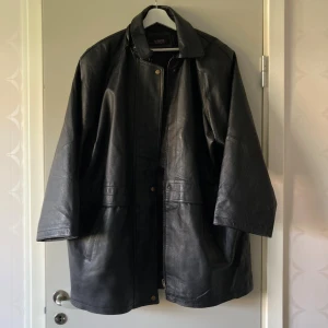 Svart skinnjacka från Auluna, strl 44 - Säljer en svart skinnjacka från Auluna Leather Company i storlek 44. Jackan har klassisk krage, dragkedja framtill och tryckknappar. Dessutom är den lätte fleecefodrad. Modellen är lite längre och har en loose passform, perfekt för dig som gillar en avslappnad stil. 