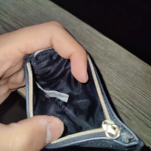 Glittrig svart plånbok från Jimmy Choo - Snygg och kompakt plånbok från Jimmy Choo med glittrig svart yta och guldfärgad logga framtill. Plånboken har dragkedja upptill och är perfekt för kort och småsaker. Stilren och lyxig accessoar som sticker ut i väskan.