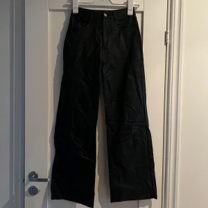 Svarta vida byxor i skinnimitation S - Säljer ett par svarta byxor i skinnimitation med hög midja och raka, vida ben. Byxorna har klassiska fickor fram och bak samt dragkedja och knapp framtill. Storlek S 