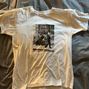 Vit t-shirt med vintage-tryck från Bvaldi - Vit t-shirt från Bvaldi med ett stort svartvitt vintage-fototryck på bröstet där det står 'Birra Peroni'. Klassisk rund hals och korta ärmar. Perfekt för dig som gillar retrostil och coola prints.