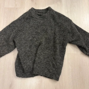 Mörkgrå stickad tröja Gina Tricot - Mysig mörkgrå stickad tröja från Gina Tricot med rund halsringning och lång ärm. Perfekt för kyliga dagar och enkel att matcha med jeans eller kjol. Tröjan har en lite loose passform och är superbekväm.