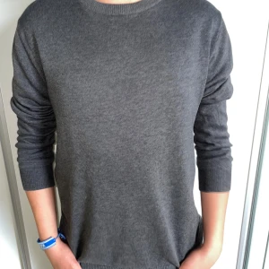 Mörkgrå bomullströja från Dressmann - En stilren mörkgrå tröja från Dressmann i mjuk pima bomull. Tröjan har rund halsringning, ribbade muddar och lång ärm. Perfekt för lager-på-lager och enkel att matcha med jeans eller chinos.