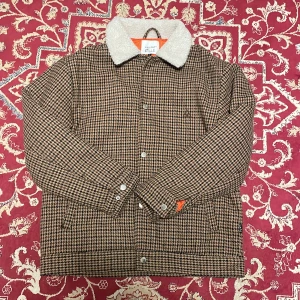 Rutig teddyjacka  - Snygg rutig teddyjacka från Vaillent med brun och svart hundtandsmönster. Jackan har en fluffig vit krage i teddy, knappar framtill och broderad logga på bröstet. Perfekt för dig som vill sticka ut med en klassisk men trendig look.