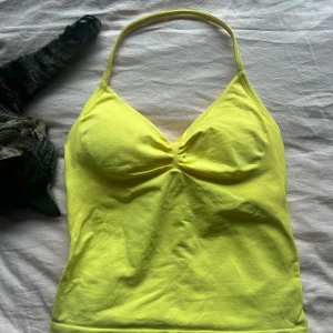 Gul halterneck träningslinne - Snygg gul halterneck linnetopp med vadderade kupor och lätt rynkdetalj framtill. Toppen har smala axelband och inbyggd bh, inga defekter 