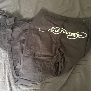 Grå cargobyxor från Ed Hardy - Säljer ett par grå cargobyxor från Ed Hardy med stora fickor och coola spänndetaljer. Sjukt fräscha! Unika o knappt använda alls. 