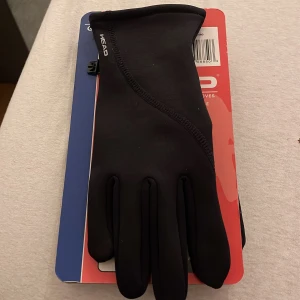 Svarta löparhandskar från HEAD - Svarta löparhandskar från HEAD med touchfunktion och silikonmönstrad insida för extra grepp. Tillverkade i stretchig fleece som sitter tajt och bekvämt på handen. Perfekta för dig som vill kunna använda mobilen utan att ta av handskarna.