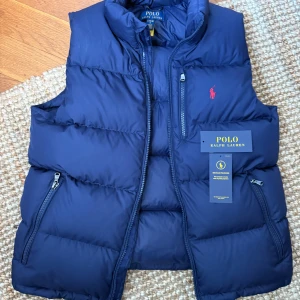 Polo Ralph Lauren dunväst - Jag säljer en riktigt snygg mörkblå dunväst från Ralph Lauren. Modellen heter Kids Quilted Down Vest. Storlek L junior (14-16 år). Xs/S i vuxenstorlek. Den är i nyskick! och lapparna finns kvar.Nypris 2695 kr