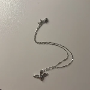 Silverhalsband med hjärta och vingar - Snyggt halsband i silverfärg med ett coolt hängsmycke format som ett hjärta med vingar. Kedjan är tunn och smidig, perfekt för att ge din outfit en unik touch. Passar dig som gillar detaljer med lite edge och symbolik.