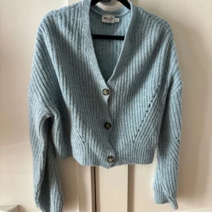 Ljusblå stickad kofta från NA-KD - Blå stickad kofta från NA-KD med v-ringning och tre stora knappar framtill. 