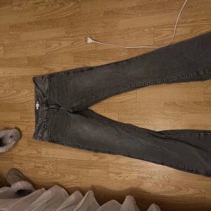 Grå jeans från Gina Tricot, storlek 170 - Säljer ett par grå jeans från Gina Tricot i storlek 170. Byxorna har raka ben, klassisk femficksdesign och snygga bakfickor med lock och knapp. Jeansen är i ett mjukt denimtyg och har en lite tvättad look. Endast en liten defekt på nedre byxan