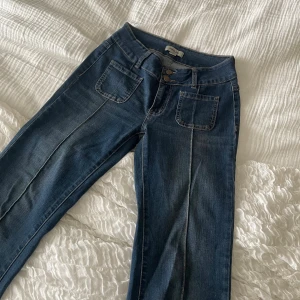 Blå jeans med utsvängda ben från Madlady - Snygga blå jeans från Madlady med raka ben och hög midja. Jeansen har två stora framfickor, dubbla knappar i midjan och markerade sömmar längs benen. Endast använda en gång. Perfekt för de under 160 som vill att byxorna ska sluta en bit nedanför ankeln. 