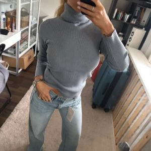 Blå ribbad polotröja - Supersnygg blå polotröja med ribbad struktur och lång ärm. Tröjan har en tight passform och hög krage som ger en clean och modern vibe. Perfekt att styla med jeans eller kjol för en chill look.