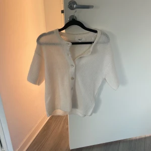 Vit stickad kofta med knappar - Superfin vit stickad kofta med korta ärmar och ribbad struktur. Snygga knappar framtill och diskret grå detalj vid axlarna. Perfekt för dig som gillar en chill och stilren look. Passar till både jeans och kjol. Helt ny aldrig använd