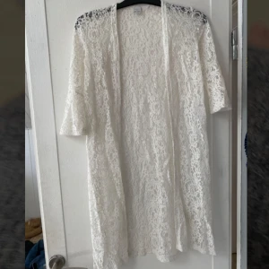 Vit spetskofta med trekvartsärm - Säljer en vit långkofta i spets med trekvartsärmar. Den har ett romantiskt mönster och är lätt transparent tack vare det tunna spetsmaterialet. Perfekt för dig som gillar en feminin och stilren look. Säljes då den inte används. 90cm lång, köpt på barnavdelningen men passar mig som är 166cm lång och vanligtvis har xs.