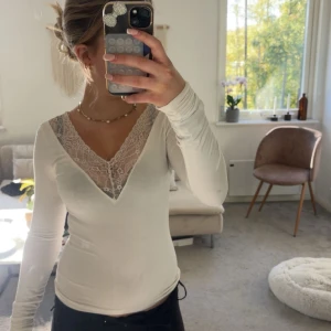 Vit långärmad topp med spets GINATRICOT - Säljer en vit långärmad topp från gina med snygg v-ringning och transparent spetsdetalj vid halsen. Modellen är slim och sitter tajt mot kroppen, perfekt för dig som gillar en feminin och stilren look. Materialet känns mjukt och stretchigt.