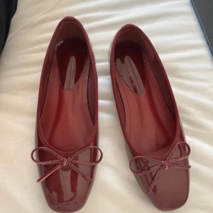 Vinröda ballerinaskor med rosett - Snygga vinröda ballerinaskor i lack med fyrkantig tå och söt rosettdetalj framtill. Skorna har en platt sula och är perfekta för dig som gillar en klassisk men trendig look. Passar till både jeans och klänning.