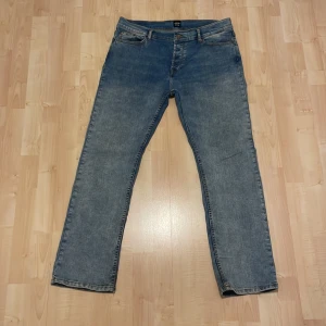 Blå jeans från Montén, rak modell - Snygga blå jeans från Montén i rak passform med klassisk femficksdesign och coola kontrastsömmar. Jeansen har en ljus tvätt och detaljerade bakfickor med zigzag-mönster. Perfekta för en avslappnad och stilren look.