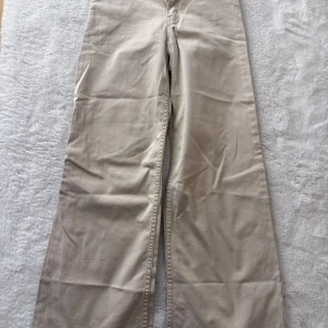 Beiga wide byxor i bomull - Säljer ett par beiga byxor med breda ben och hög midja. Byxorna är tillverkade i mjuk bomull och har klassiska bakfickor. Perfekta för en chill och stilren look.