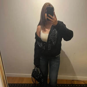 Svart hoodie  - Säljer en svart hoodie med dragkedja och coola strassdetaljer i form av ett skelettmönster på framsidan. Perfekt för en edgy look! Skriv vid frågor💗