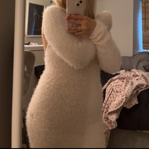 Fluffig ljusrosa klänning med öppen rygg - Superfin fluffig ljusrosa klänning från Chiquelle. Tight passform, långärmad och kort modell. Klänningen har öppen rygg med snygg knytning och är gjord i ett mjukt, stickat material som känns lyxigt och mysigt. Perfekt för dig som vill sticka ut med en unik look!