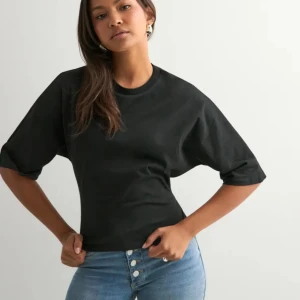 Svart omlottopp med knyt i ryggen - Svart topp i bomull med rund hals och halvlånga ärmar. Toppen har öppen rygg och knyts med långa band baktill för en snygg omlotteffekt. Perfekt till jeans eller kjol för en trendig look.