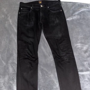 Svarta jeans från Lee - Säljer ett par svarta jeans från Lee med klassisk femficksdesign och raka ben. Jeansen har en snygg, enkel look och Lee-loggan syns på linningen. Perfekta för dig som gillar stilrena och tidlösa byxor. Storlek 32/32. Modell: Luke. 