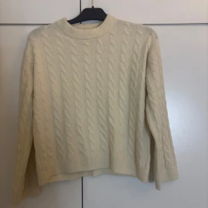 Krämvit kabelstickad tröja H&M XS - Krämvit kabelstickad tröja från H&M i storlek XS. Tröjan har rund halsringning, ribbade muddar och ett klassiskt flätmönster över hela plagget. Perfekt för lager-på-lager och en clean look.