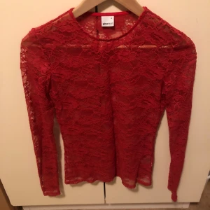 Röd spetsblus från Gina Tricot - Säljer en snygg röd spetsblus från Gina Tricot. Blusen är genombruten med vackert spetsmönster, har rund halsringning och långa ärmar. Perfekt för dig som vill sticka ut med en färgstark och feminin look.