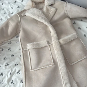 Beige teddyjacka från Amisu - Säljer en beige teddyjacka från Amisu med stora fickor och mysigt fuskpälsfoder. Jackan har bred krage med spänne, knappar framtill och detaljer i samma färg. Perfekt för kalla dagar och riktigt snygg till alla outfits.