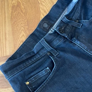 Mörkblå jeans Tiger of Sweden 28/32 - Snygga mörkblå jeans från Tiger of Sweden i modellen Shine. Klassisk femficksdesign, raka ben och normal passform. Jeansen är tillverkade i mjukt denimtyg och har diskreta detaljer med svarta nitar och knapp. Perfekta för en stilren look.