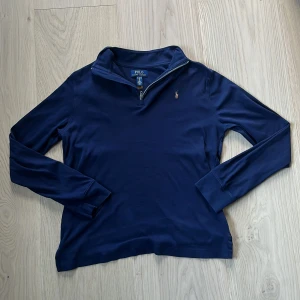 Marinblå half zip från Polo Ralph Lauren - Marinblå långärmad tröja från Polo Ralph Lauren med half zip och klassisk krage i tunt material. Tröjan har en liten broderad logga på bröstet. Storlek XL 18-20