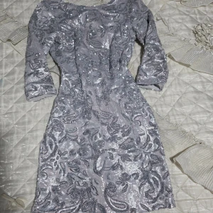 Glittrig silverklänning från Bik Bok - Snygg kort silverfärgad klänning från Bik Bok i storlek S, täckt med glittriga paljetter och ett detaljerat mönster. Klänningen har trekvartsärmar och en rundad halsringning samt en djupare rygg. Perfekt för dig som vill sticka ut med en glittrig look.