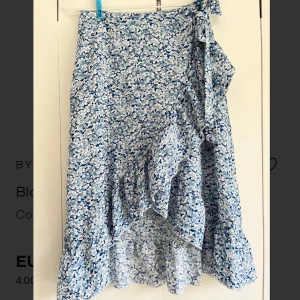 Blå blommig omlottkjol med volang - Supersöt blå omlottkjol med vitt blommönster och volangkant. Kjolen har knyt i sidan och en lätt vågig form, super fin på sommaren och passar till allt🩵🌸✨ HELT NY OCH OANVÄND 