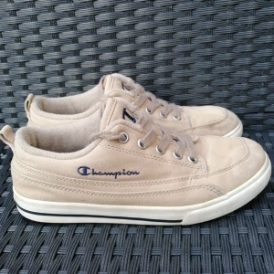 Beige sneakers från Champion, strl 36 - Snygga beige sneakers från Champion i canvas med klassisk snörning och vit sula med svart rand. Ikonisk Champion-logga broderad på sidan och tryckt på plösen och hälen. Perfekta för en avslappnad streetstyle-look.