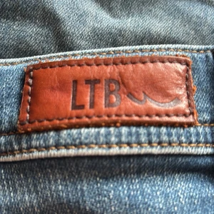 Blå jeanskjol från LTB - Snygg blå jeanskjol från LTB med klassisk femficksdesign, bälteshällor och slitna detaljer. Kjolen har en kort passform och är tillverkad i robust denim med snygga kontrastsömmar. Perfekt för dig som gillar en avslappnad och trendig stil.