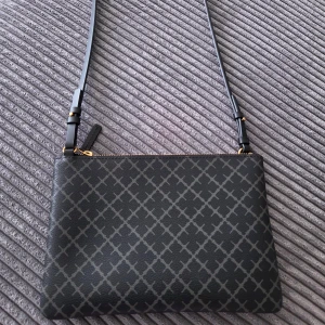 Svart axelväska från By Malene Birger - Snygg svart axelväska från By Malene Birger med justerbar rem och guldfärgad dragkedja. Väskan har ett stilrent rutigt mönster i grått och är tillverkad i tåligt syntetmaterial. Perfekt storlek för det viktigaste och en clean look.