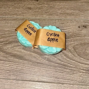 Grönt äpple tvål - Två runda tvålar med doft av grönt äpple, ljusblå färg och dekorerade med vågig yta. Förpackade med brunt pappersband där det står 'Grönt äpple' handskrivet. 