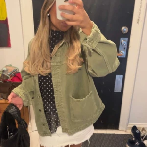 Grön jeansjacka - Säljer en grön jeansjacka med stora fickor framtill och knappar längs hela framsidan. Jackan har en loose passform och är perfekt att slänga över en outfit för en chill vibe. Passar dig som gillar streetstyle och avslappnat mode.