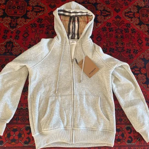 Grå Burrbery half zip hoodie - En skön och snygg grå Burrbery half zip hoodie som är nästan helt ny. Fick den som present men är icke min storlek. S men passar som xs har. Har inget märke eftersom de gamla modellen
