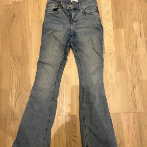 Blå bootcut jeans från Gina Tricot - Bootcut jeans i klassisk blå tvätt från Gina Tricot. Modellen har fem fickor, dragkedja och knapp framtill samt bälteshällor. Jeansen har en snygg utsvängd passform och är tillverkade i jeansmaterial med lätt slitning för en cool look.