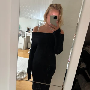 Svart offshoulder stickad klänning - Svart, ribbstickad klänning med offshoulder och långa ärmar. Sitter tight och har en snygg, enkel design som framhäver axlarna. Perfekt för dig som gillar stilrena och trendiga plagg. Supermjuk och skön att bära.