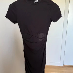 Svart ribbad kortklänning Divided H&M - Svart ribbad kortklänning från Divided H&M i tight passform. Klänningen har korta ärmar och coola mesh-detaljer i midjan som ger en edgy look. Perfekt för dig som gillar minimalistisk stil med en twist.