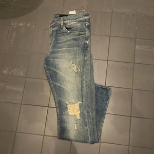 Tiger of sweden jeans - Snygga blå jeans med coola slitningar och en klassisk femficksdesign. Tillverkade i Italien med en stilren läderpatch baktill. Perfekta för en avslappnad look.
