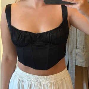 Svart satin korsettopp med breda axelband - Snygg svart korsettopp i satin med breda axelband. Strl s. Toppen är i använt skick💖