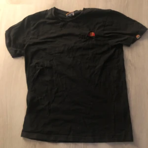Svart t-shirt från Ellesse - Svart t-shirt från Ellesse med liten broderad logga på bröstet och ärmen. Klassisk rund hals och rak passform. Tillverkad i mjuk bomull, perfekt för en avslappnad stil.
