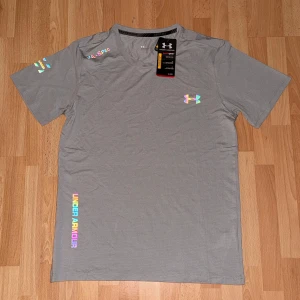 Grå Under Armour HeatGear t-shirt - Snygg grå t-shirt från Under Armour med reflekterande logga. Tillverkad i andningsbart material. Klassisk passform med korta ärmar och rund hals. Hör av dig vid fler frågor eller funderingar!