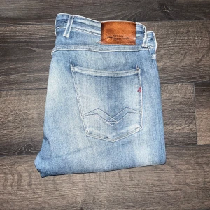 Replay Anbass jeans - Säljer ett par Replay Anbass jeans i ljusblå tvätt med slitningar och lätt distressed look. Klassisk femficksmodell med snygga detaljer på bakfickan och läderpatch i midjan. Jeansen är i stretchig bomull och har en slim passform. Midja 44cm längd 93cm.OBS OBS Jeansen är uppsydda från L34 till att motsvara L30 men kolla måtten noggrant. JAG SKICKAR INGA FLER BILDER NÄR JAG BÄR JEANSEN.