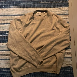 Beige bomullströja från Gant L - Klassisk beige tröja från Gant i storlek L. Tröjan har rund halsringning, diskret broderad logga på bröstet och är tillverkad i mjuk bomull. Perfekt för lager-på-lager och enkel att matcha med jeans eller chinos.